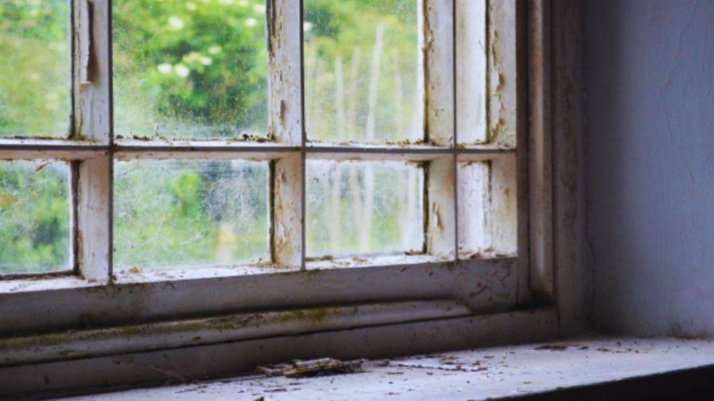 An image of a weathered window with a cracked frame showing visible dirt and grime.