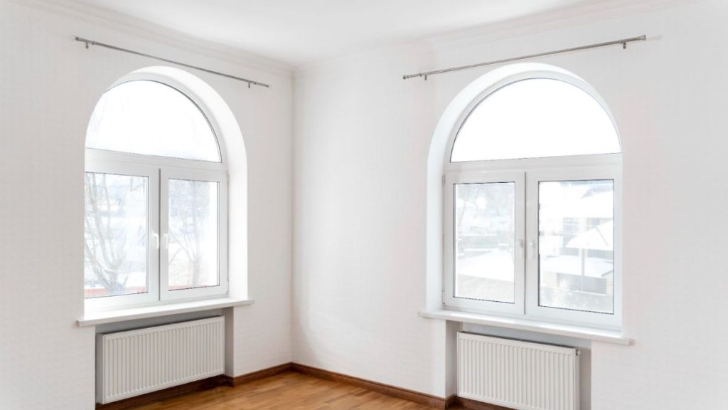 An empty room featuring two windows and a polished wooden floor, creating a bright and spacious atmosphere.