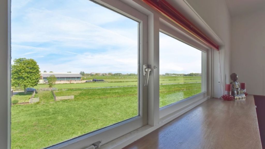 A serene view of a lush green field framed by a window in a cozy house, inviting nature indoors.