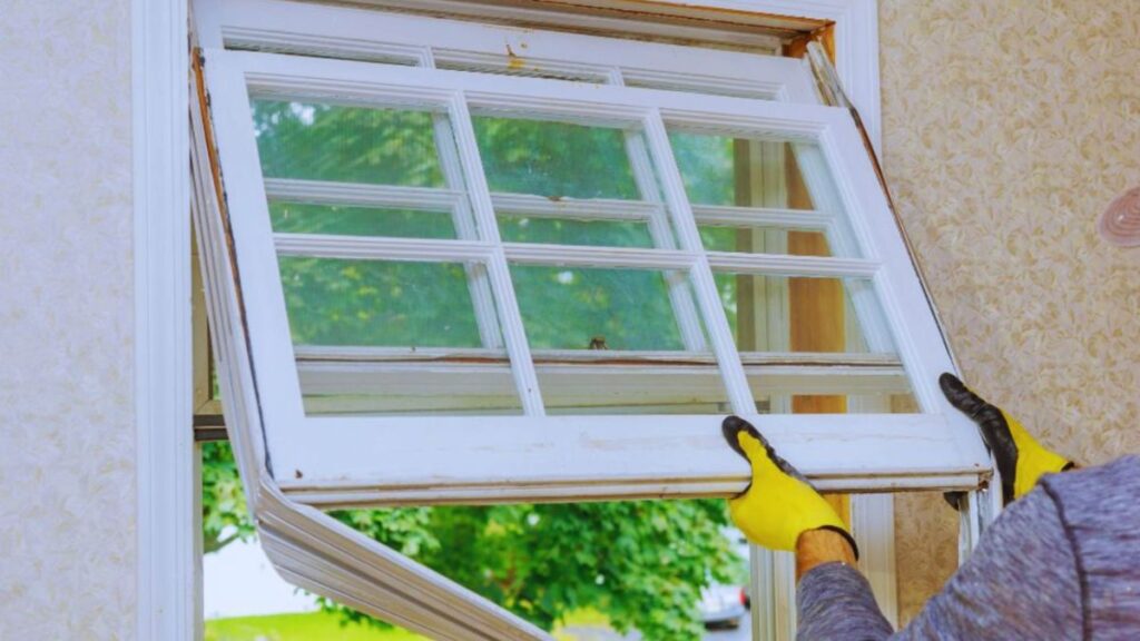 A man in a yellow glove is engaged in installing a window, focusing his attention on detail and craftsmanship.