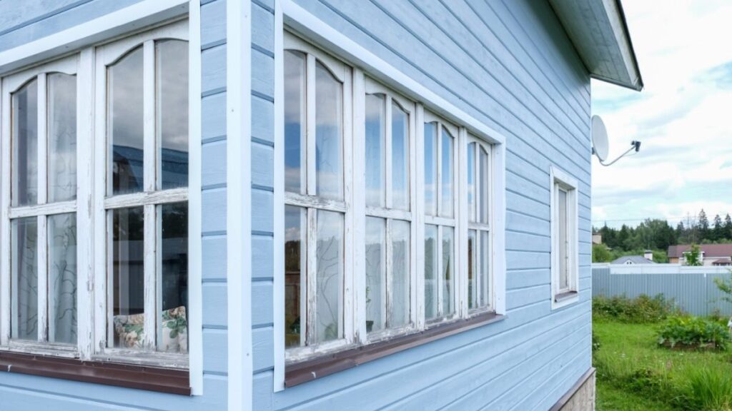 A blue house adorned with a window and a white fence, highlighting options for window types in home design.