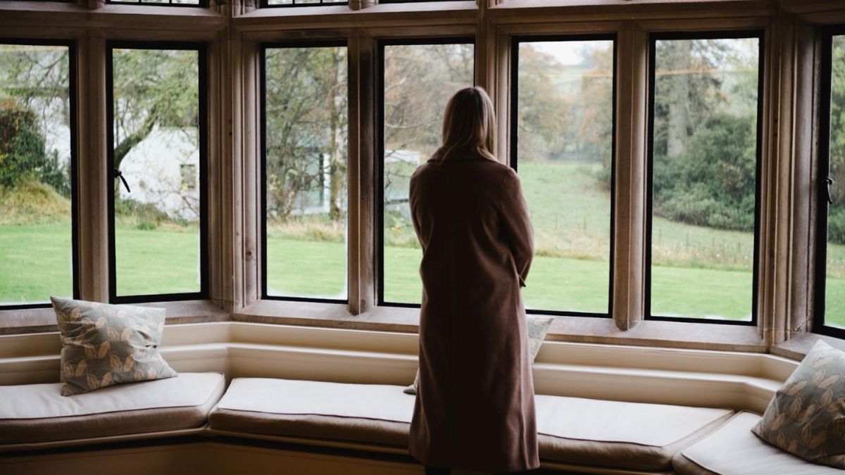 A woman gazes out a window, admiring the serene countryside view beyond, highlighting the beauty of bay and bow windows.