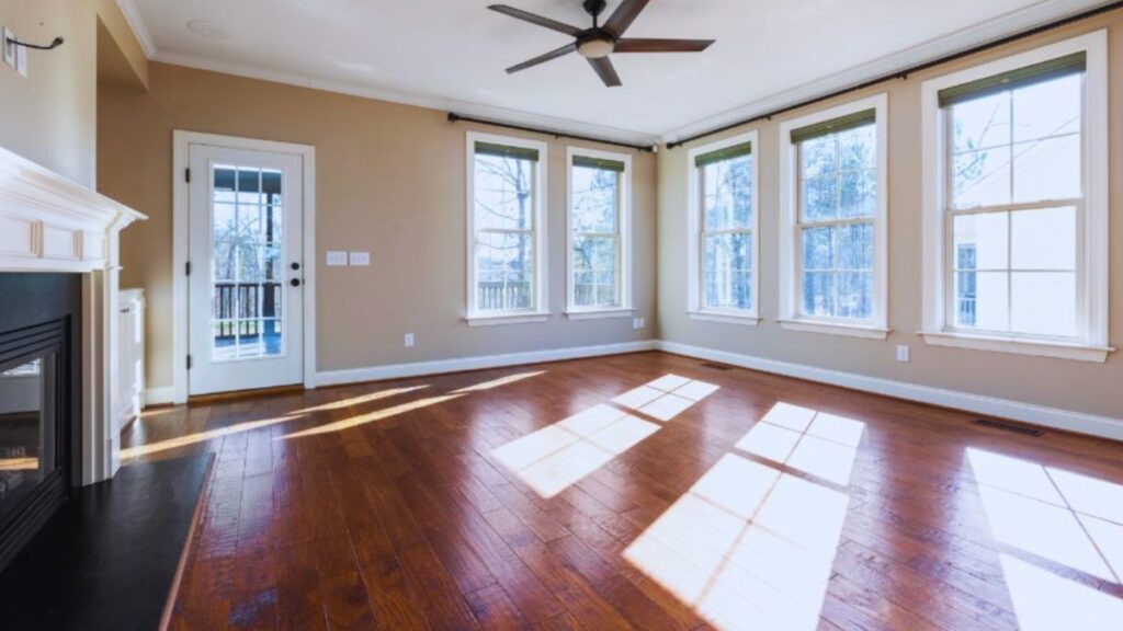 Bright living room with double-hung windows, white trim, hardwood flooring, a ceiling fan, a fireplace, and a glass door to the deck.