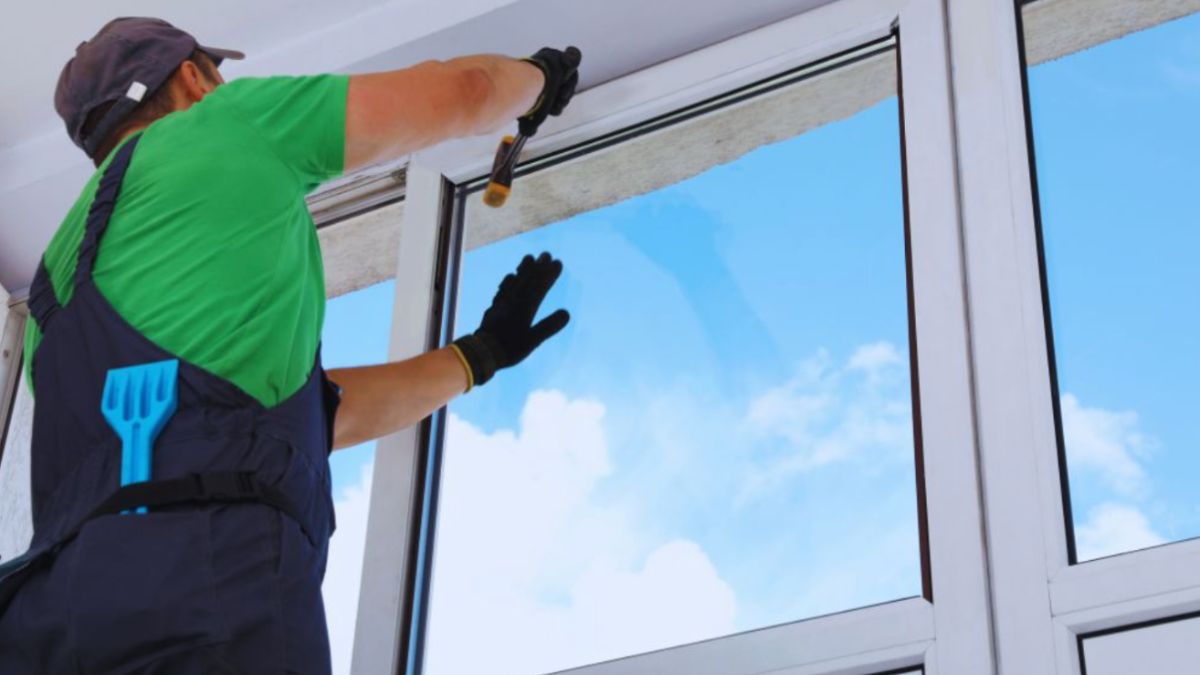 A man in blue overalls and a hat installs a double-hung window, demonstrating skilled craftsmanship and attention to detail.