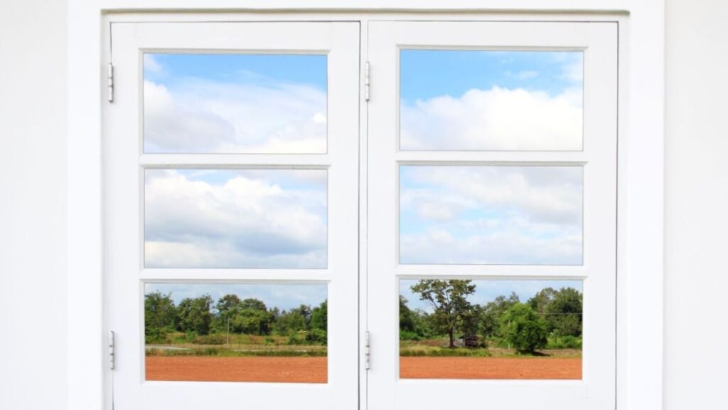 A white double-hung window opens to a peaceful vista of a lush field, inviting the outdoors in.