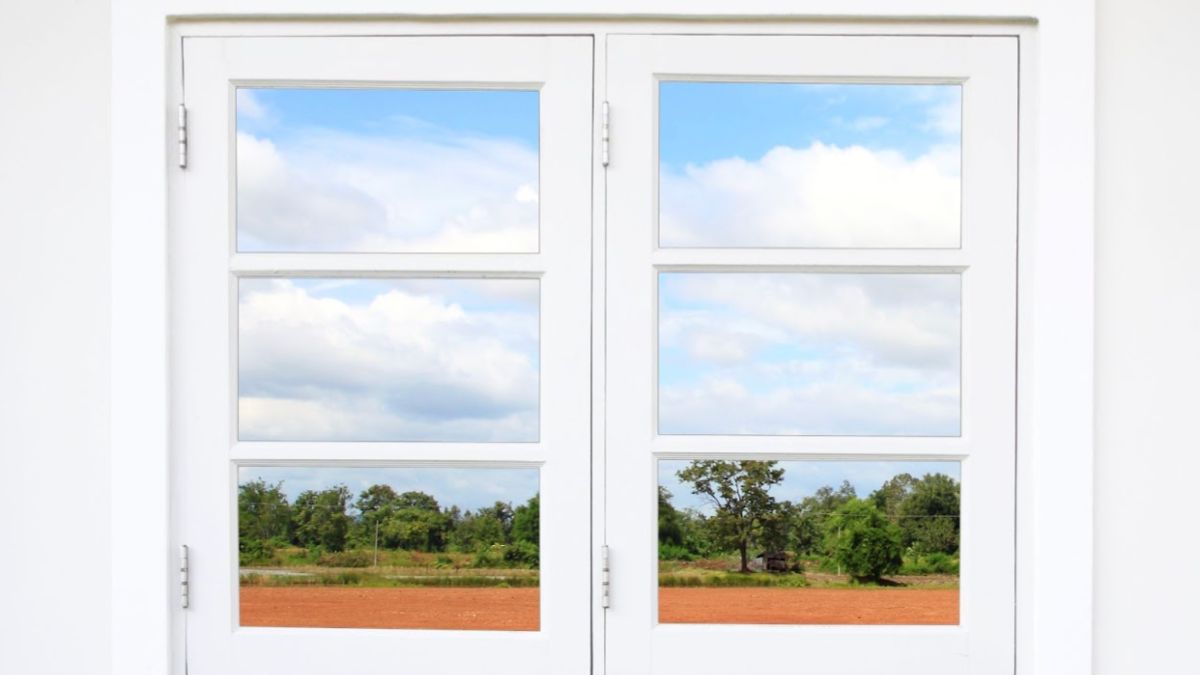 A white double-hung window opens to a peaceful vista of a lush field, inviting the outdoors in.