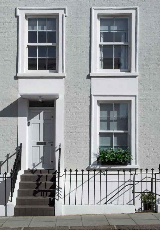 A charming white brick townhouse featuring single-hung windows, a stylish gray front door, and elegant black wrought iron railings.