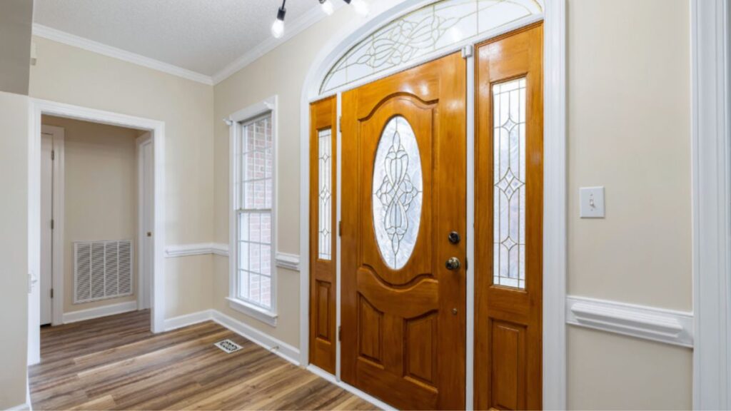 A hallway featuring a wooden door and an elegant light fixture showcasing transom windows and sidelights for added style.