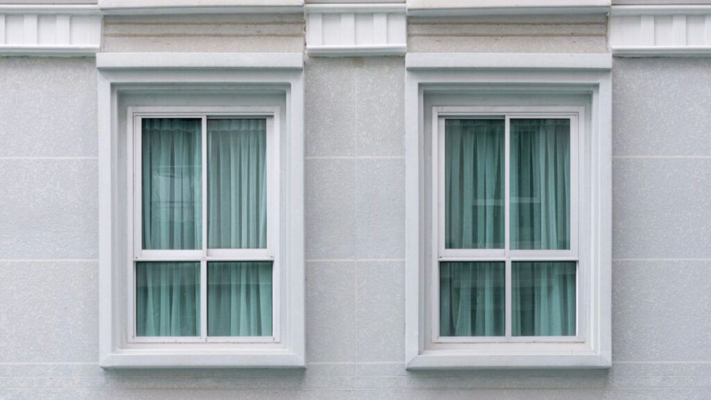 Two windows with green shutters adorn a white facade, demonstrating professional window installation.