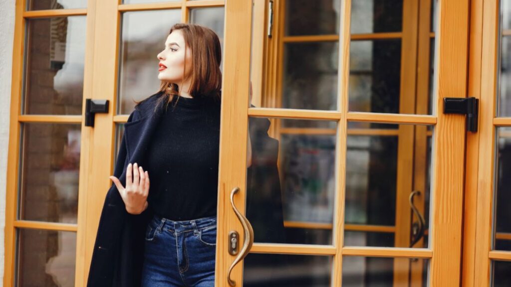 A woman stands before a brown door, contemplating the transformative benefits of door replacement by HHI Windows and Doors.