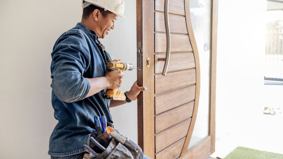 A person in a denim shirt and hard hat using a drill on a wooden door during a professional door replacement process.