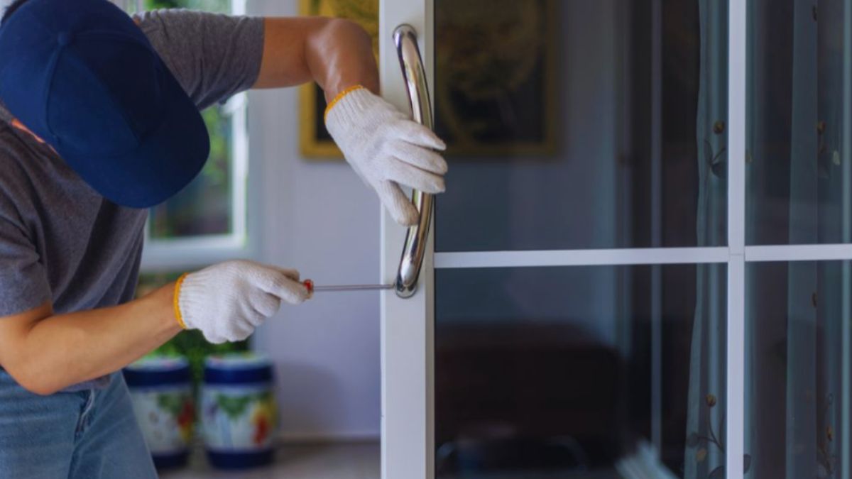 A man dressed in a hat and gloves is fixing a glass door during a door replacement.