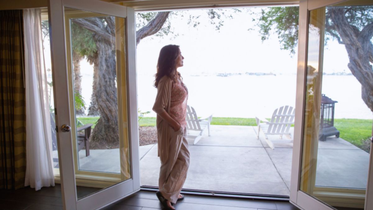 A woman stands confidently in front of patio doors, framed by natural light and a welcoming outdoor view.