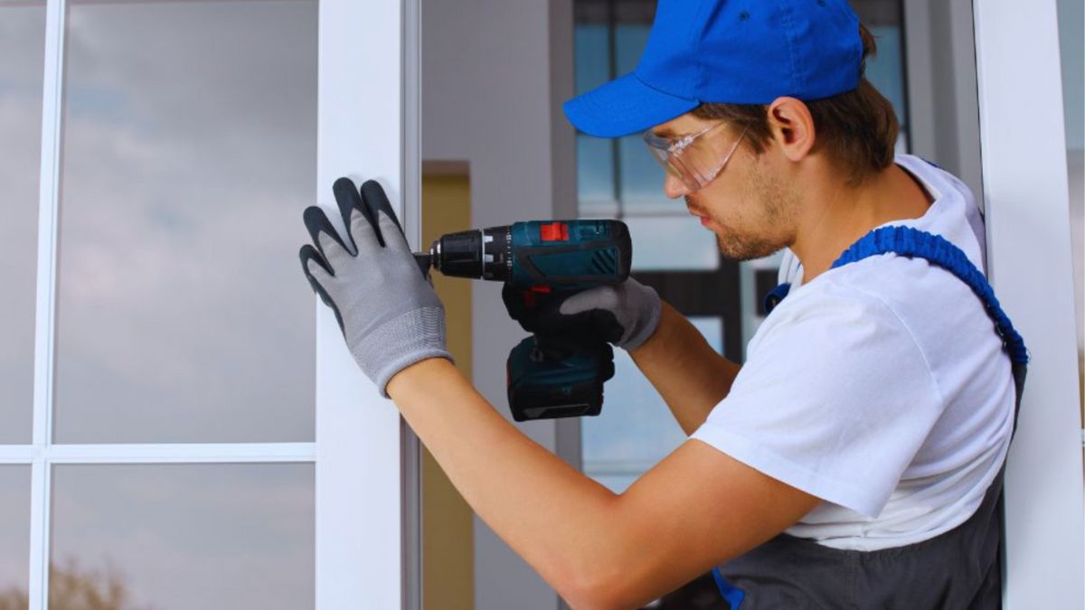 A man in blue overalls and gloves drilling into a door during the replacement process, illustrating professional door installation.