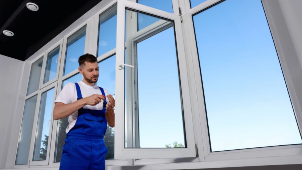 A man wearing blue overalls is installing a window.