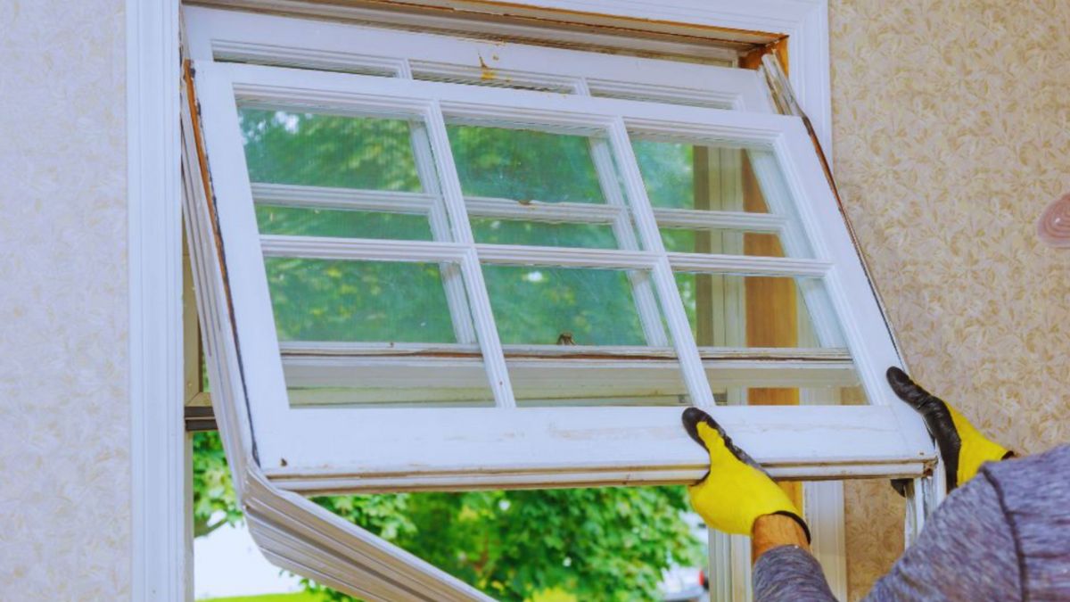 A man wearing a yellow glove repairs a window during a replacement.