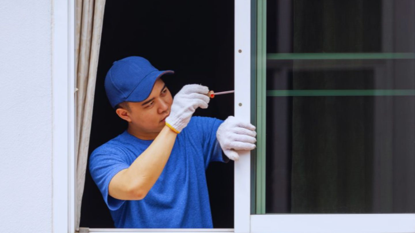 Window replacement in progress as a worker in a blue shirt and cap uses a screwdriver to install or adjust a window frame.